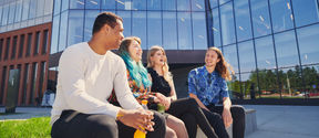 School of business students sitting in front of the campus and laughing